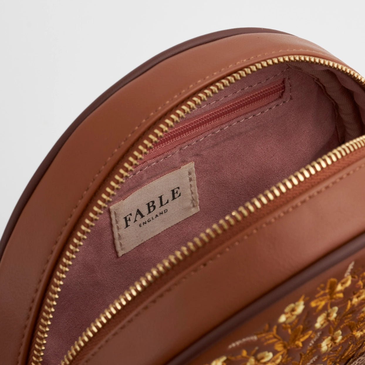Brown leather bag with floral embroidery and 'Fable' label on a light gray background