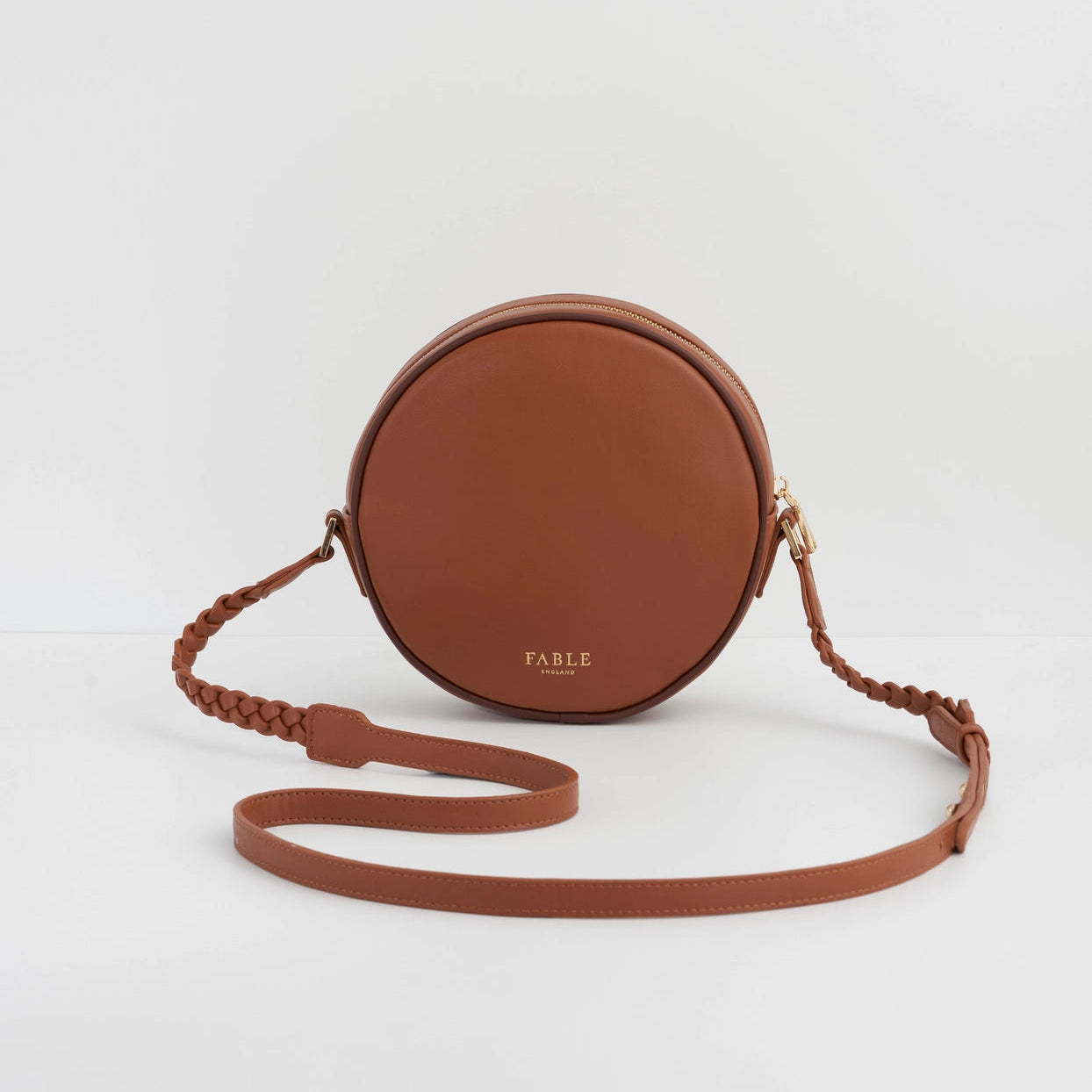 Brown round crossbody bag with a strap on a light gray background