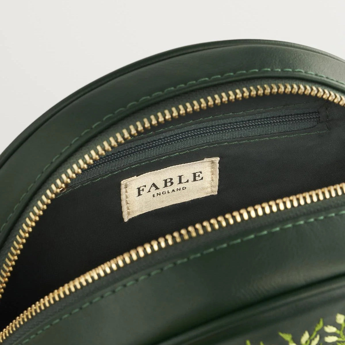 Green bag with gold zipper and 'Fable' label on a light gray background
