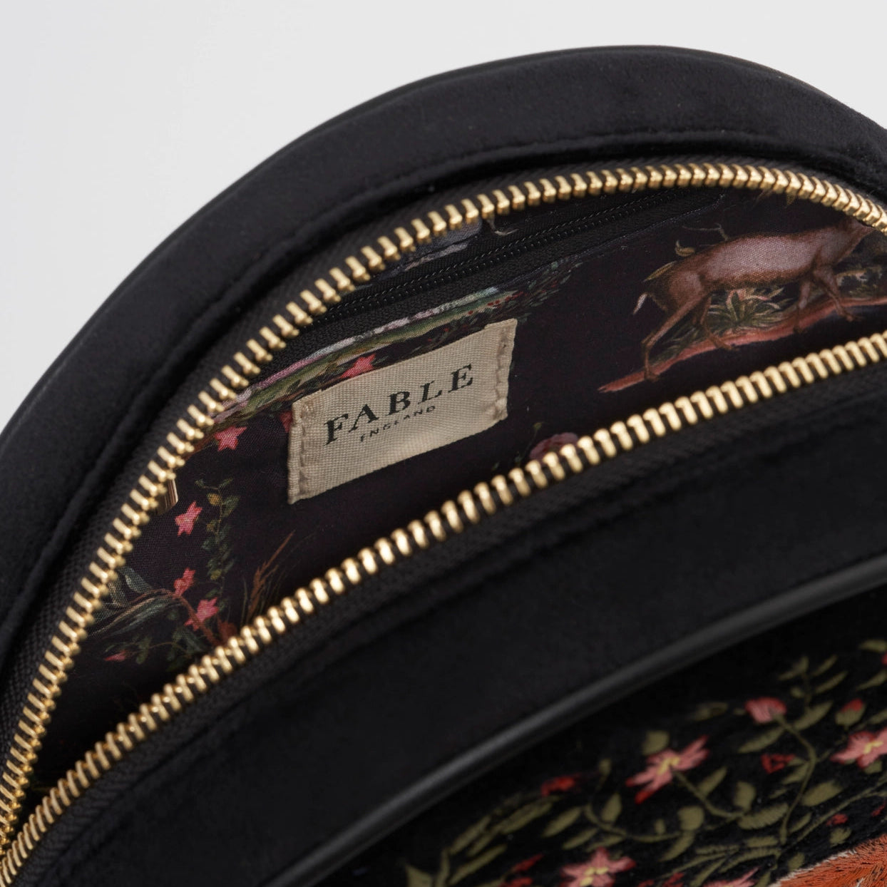 Close-up of a black bag with floral and animal embroidery and gold zipper, featuring the 'Fable' brand.