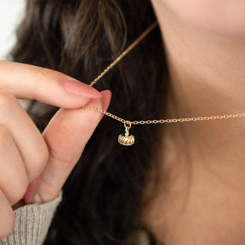 Gold necklace featuring a small gold pumpkin charm. 