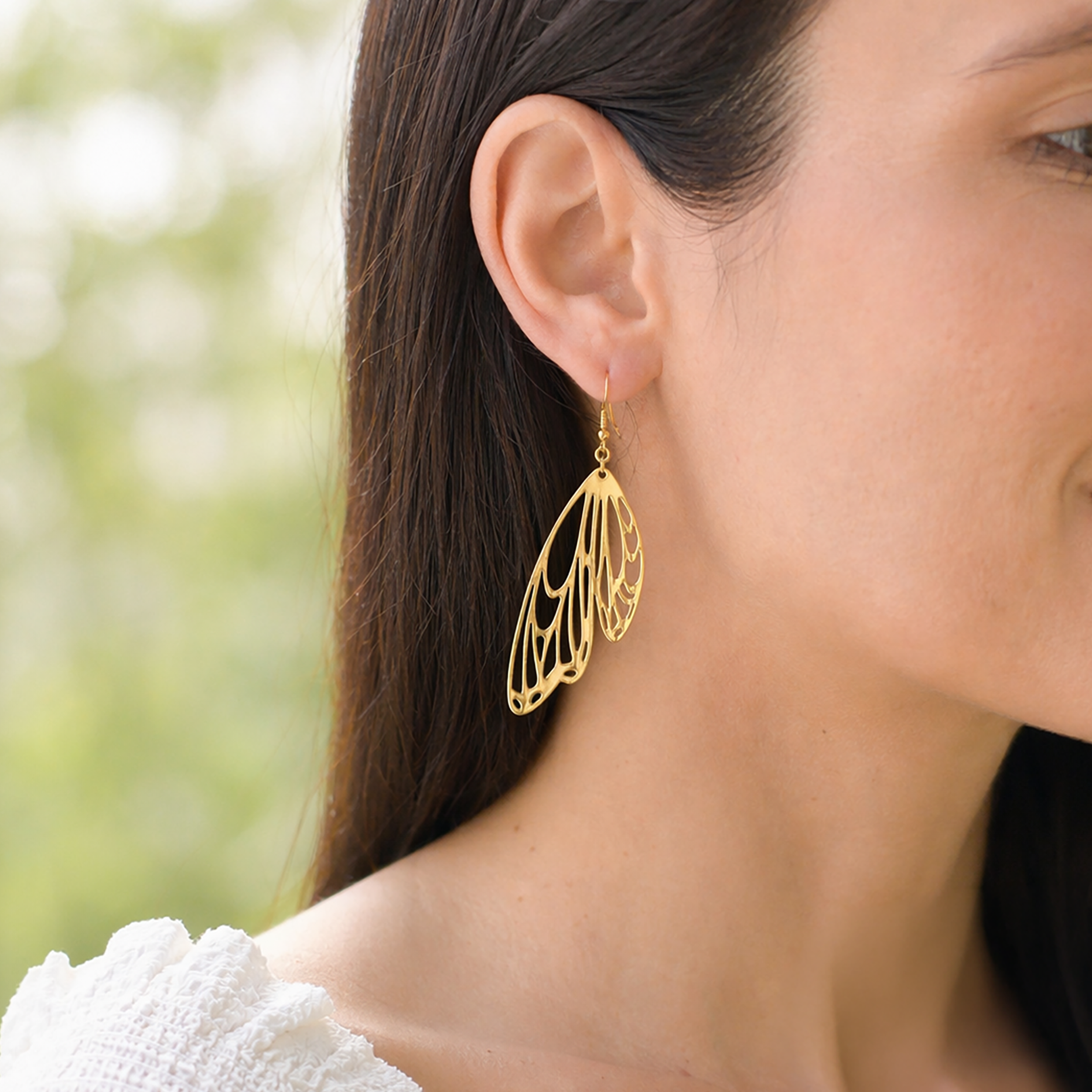 Gold butterfly-shaped earrings worn by a person with a blurred natural background