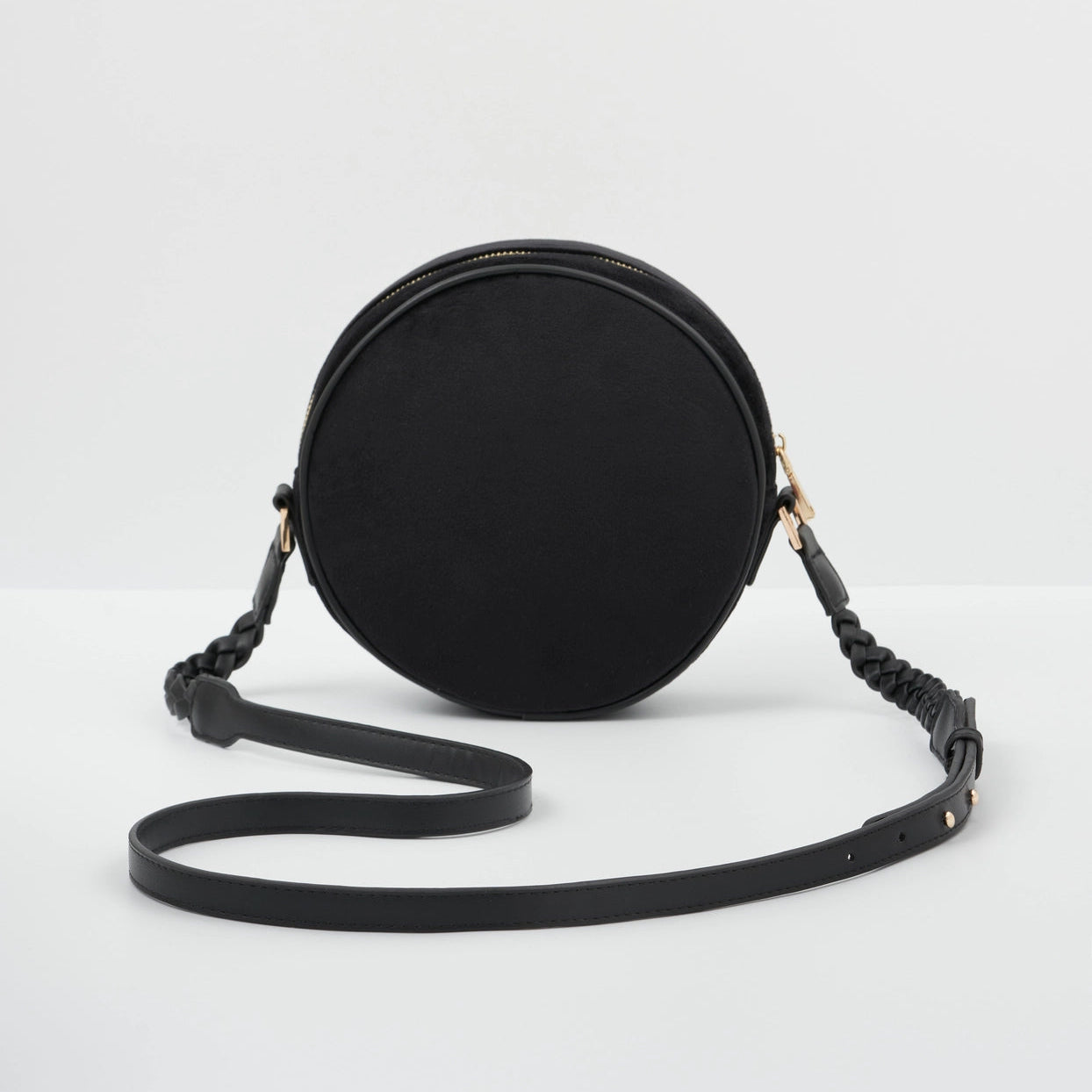 Black round crossbody bag with braided strap on a white background