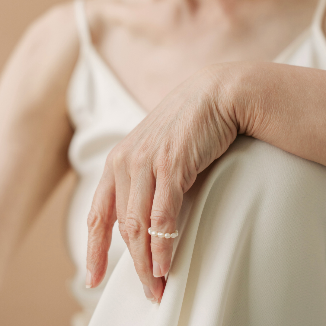 A woman's hand placed over her knee with a beaded pearl ring worn halfway up her pinky finger. 