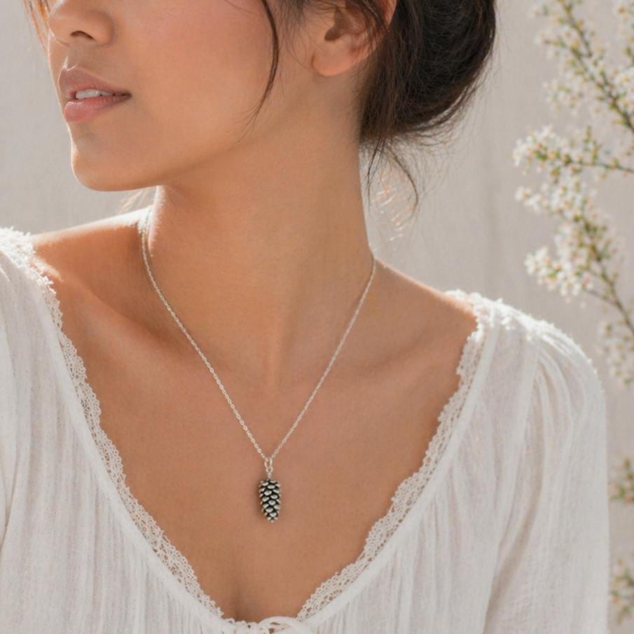 Woman wearing a silver necklace with a pinecone pendant against a neutral background