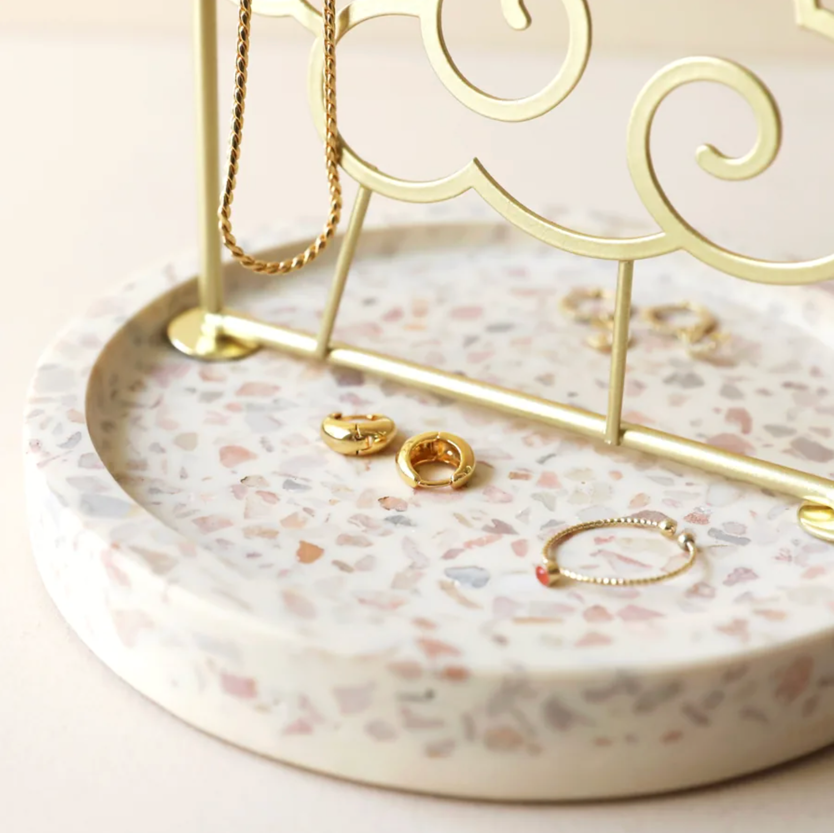 Jewelry stand with gold necklaces, earrings, and rings on a terrazzo-style tray.